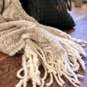 Textured beige scarf with tassels on a wooden surface