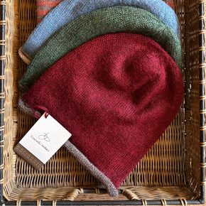 Stack of knit beanies in various colors with a visible brand tag on a woven basket background.