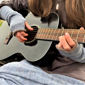 Person playing an acoustic guitar with a focus on the hands and guitar body.