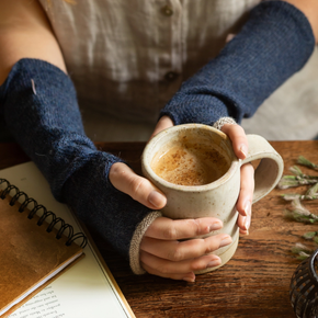 Person holding a mug of coffee on a wooden table with a notebook and plant.