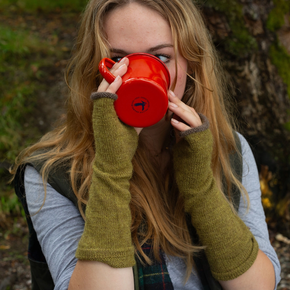 Person drinking from a red mug with green fingerless gloves in a natural setting