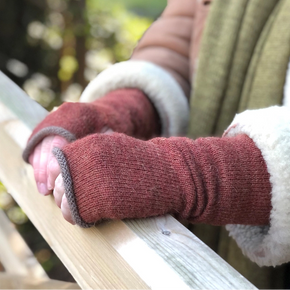 Close-up of hands wearing red orange fingerless gloves holding onto a wooden railing with a blurred natural background.
