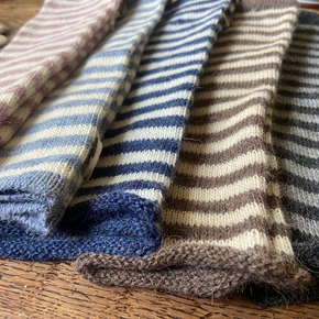 Four striped knitted wrist warmers in different colors on a wooden surface.