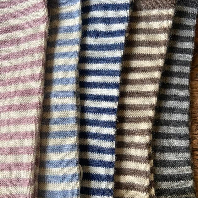 Five striped wrist warmers in various colors on a wooden surface