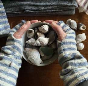 Person holding a bowl of seashells with more shells on a wooden surface