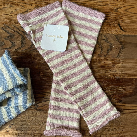 Striped knitted wrist warmers on a wooden surface with a visible brand tag.