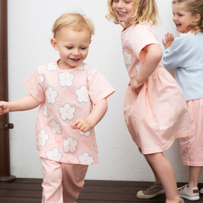 Three children in matching pink outfits with floral patterns on a wooden floor.