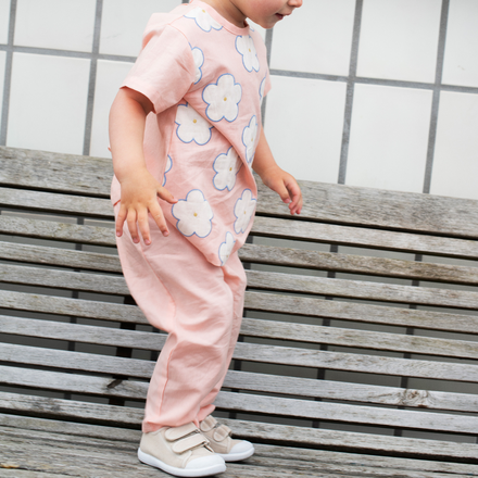 Child wearing a pink floral outfit standing on a wooden bench outdoors.