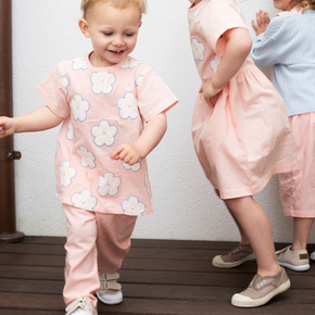 Three children in matching pink outfits with floral patterns on a wooden floor.