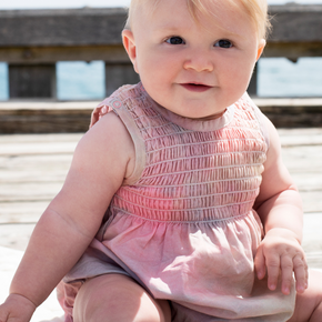 Baby in a pink onesie sitting on a wooden surface with a blurred background