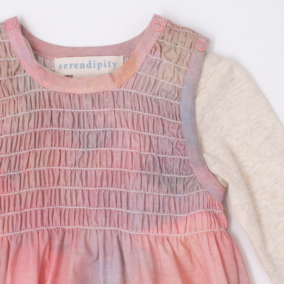Pink smocked onesie with 'serendipity' label on a white background