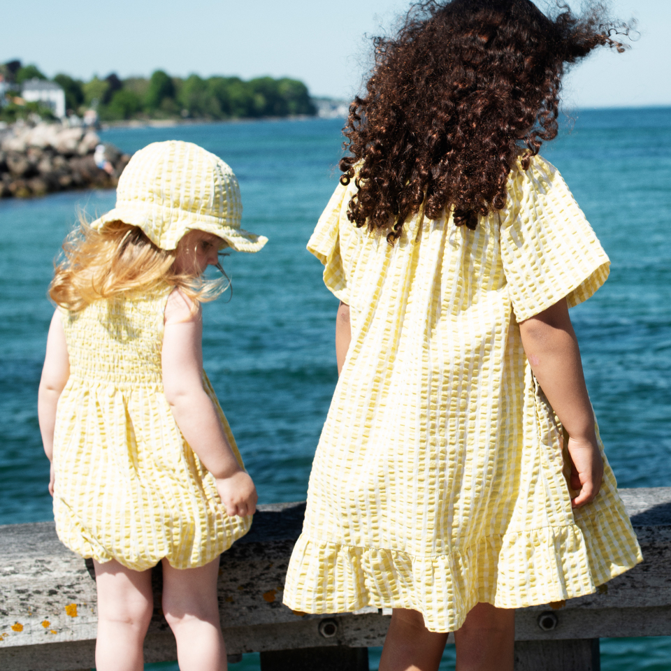Two children in yellow romper and dress standing by a waterfront