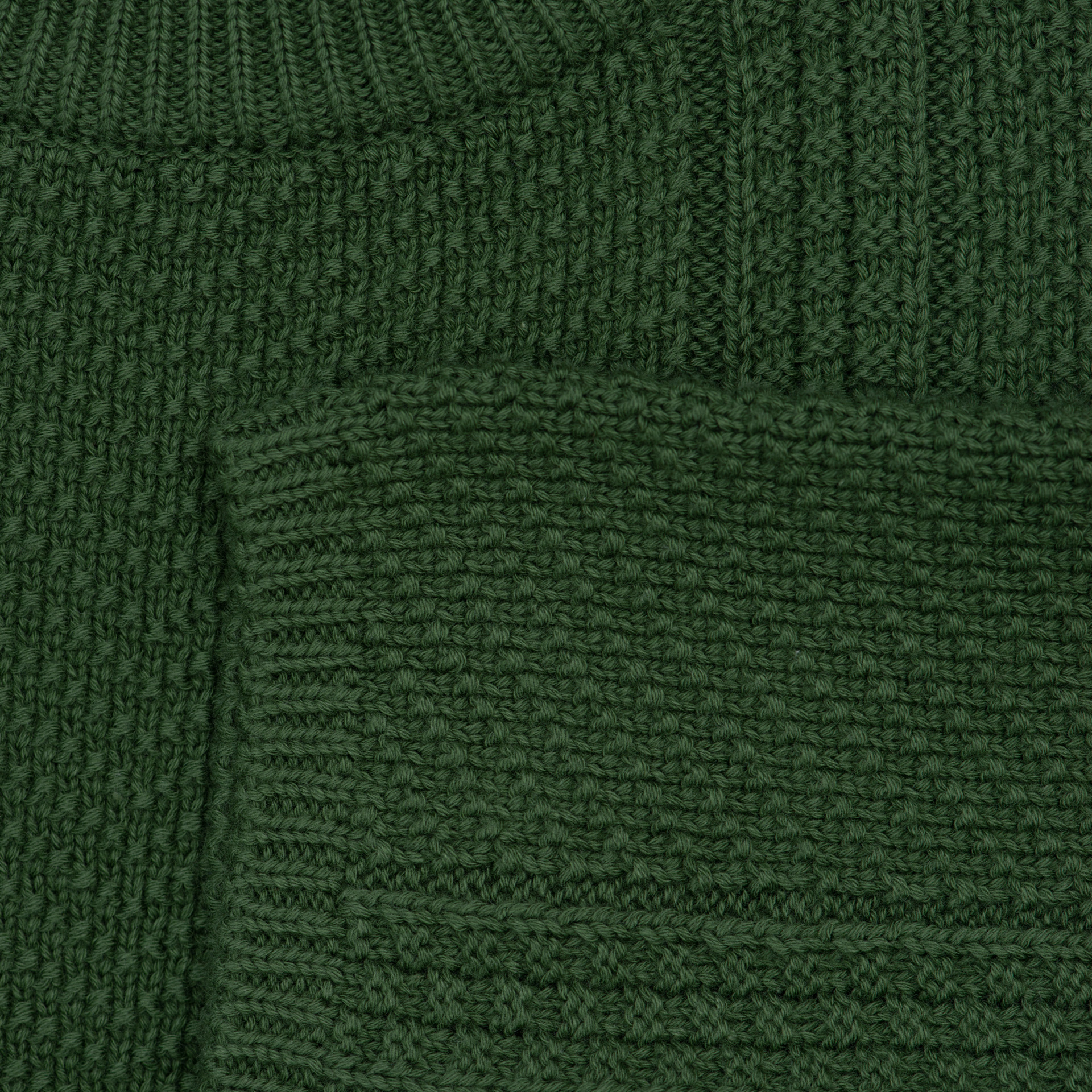 Close-up of a dark forest green ribbed knit sweater showing the texture of the fabric and a portion of the collar.