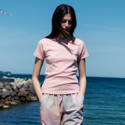 Woman wearing a pink t-shirt and colorful pants standing by the ocean.