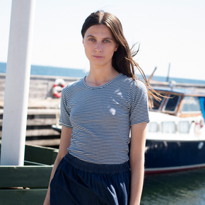 Woman wearing a striped shirt and dark pants by a marina with boats in the background