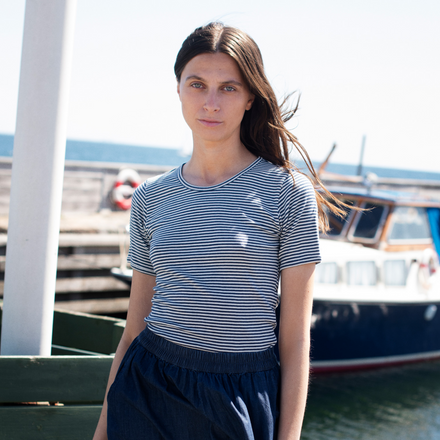 Woman wearing a striped shirt and dark pants by a marina with boats in the background