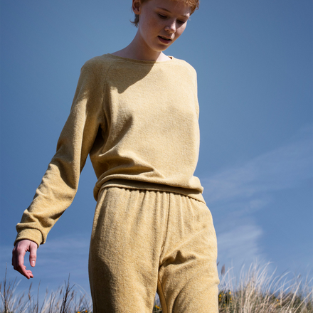 Person wearing a yellow sweater and pants standing against a blue sky.