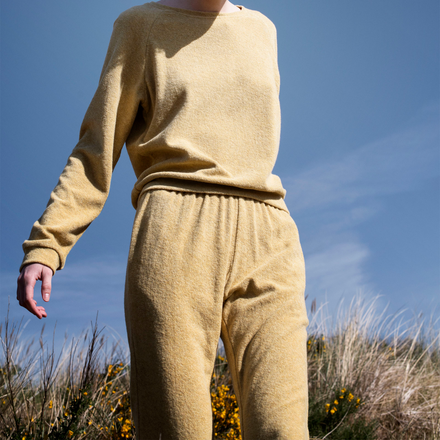 Person wearing a yellow sweater and pants standing against a blue sky.
