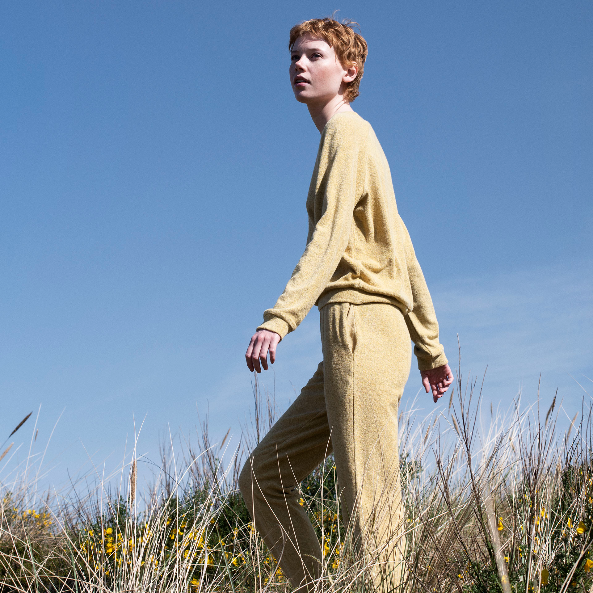Person wearing a yellow outfit standing in a field with a clear blue sky.