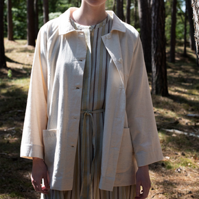 Person wearing an off white jacket over a striped dress in a forest setting