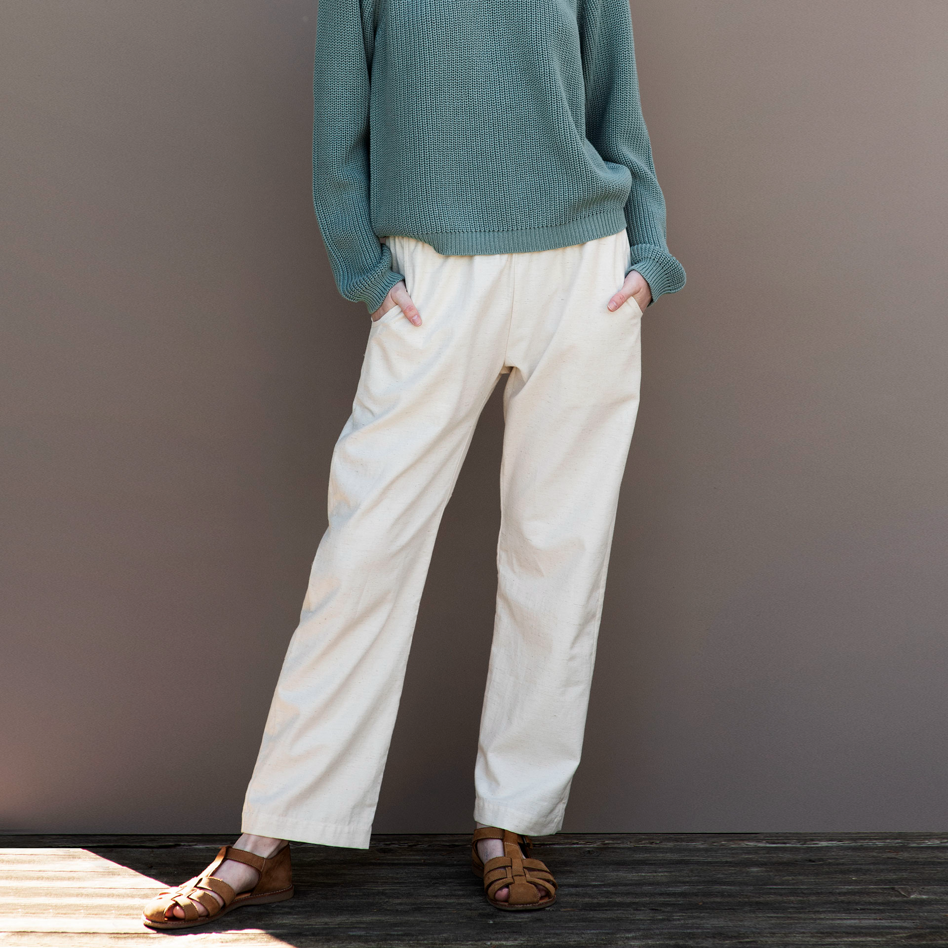 Person wearing a teal sweater and white pants against a gray background