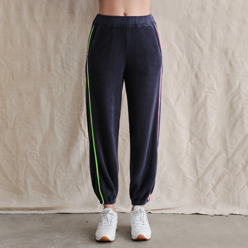 Sundry Faux Sherpa Sweatpants - model wearing navy blue sweatpants with a pink and green stripe down the outer seems and eliastic waistband and ankles on a neutral background