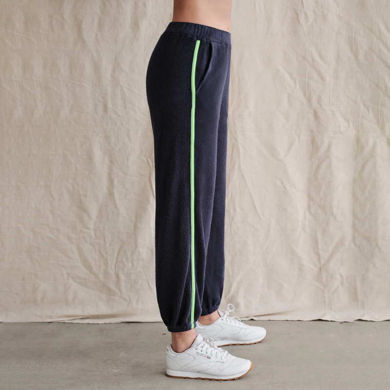 Sundry Faux Sherpa Sweatpants - model wearing navy blue sweatpants with a pink and green stripe down the outer seems and eliastic waistband and ankles on a neutral background
