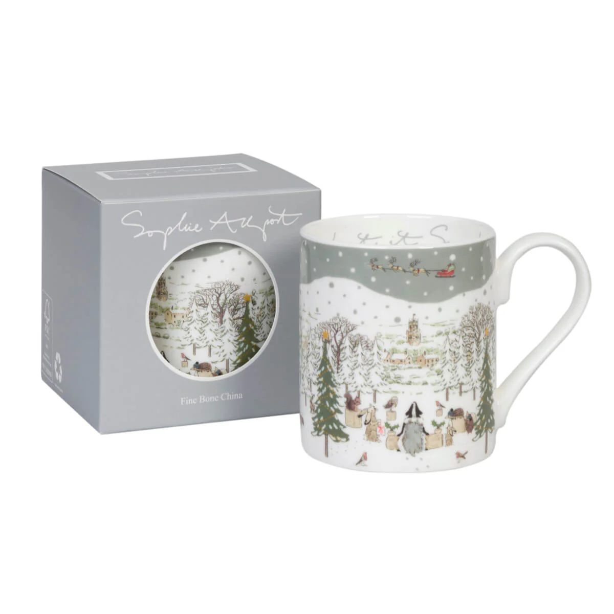 A white china mug with a winter village illustration, shown next to its gray gift box with a circular window. The mug features a snowy landscape with trees, houses, and a sleigh.