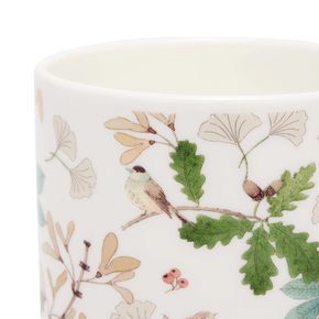 Ceramic mug with nature-themed design featuring leaves, acorns, and a bird on a white background