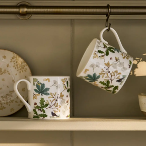 Two floral-patterned mugs hanging on a hook against a neutral wall.