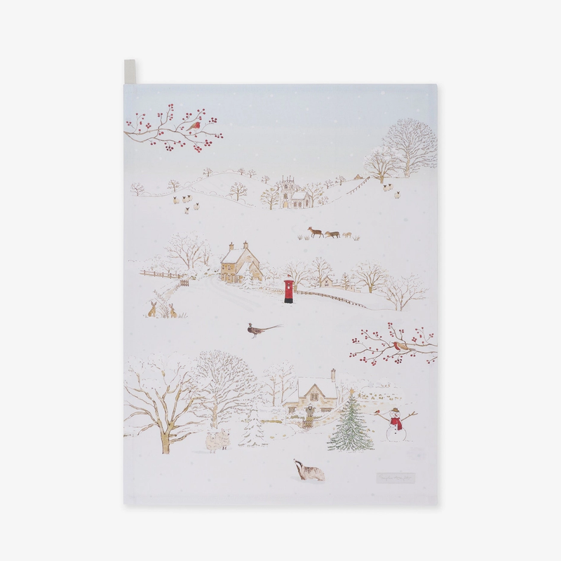 Tea towel featuring a whimsical winter village scene with snow-covered trees, small houses, a lighthouse, birds, and a few figures, shown against a plain light background.