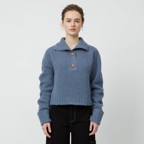 Atelier Delphine Stand Collar Jumper - model wearing slate blue sweater with folded collar, cuffed sleeves, and button closure on a neutral background