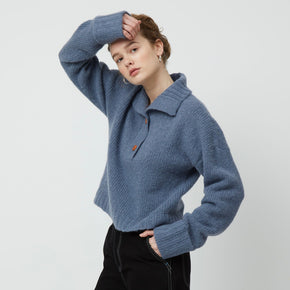 Atelier Delphine Stand Collar Jumper - model wearing slate blue sweater with folded collar, cuffed sleeves, and button closure on a neutral background