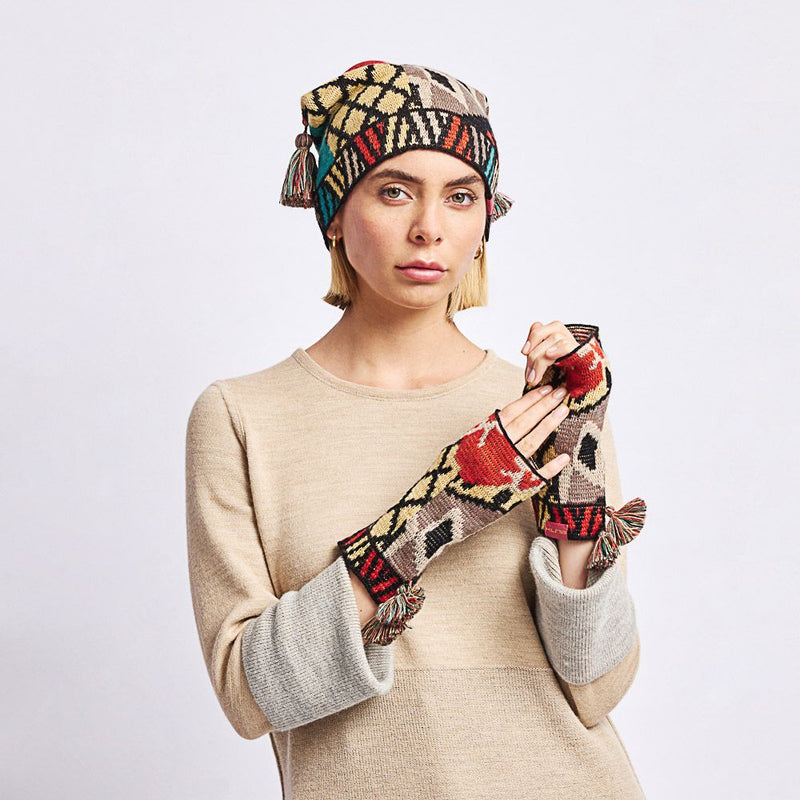 Kuna Watanabe Alpaca Gloves - model wearing yellow, black, red, and blue patterned gloves with pom pom detail on a neutral background