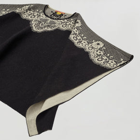 Kuna Wendy Poncho - black poncho with white lining and floral detail on a neutral background