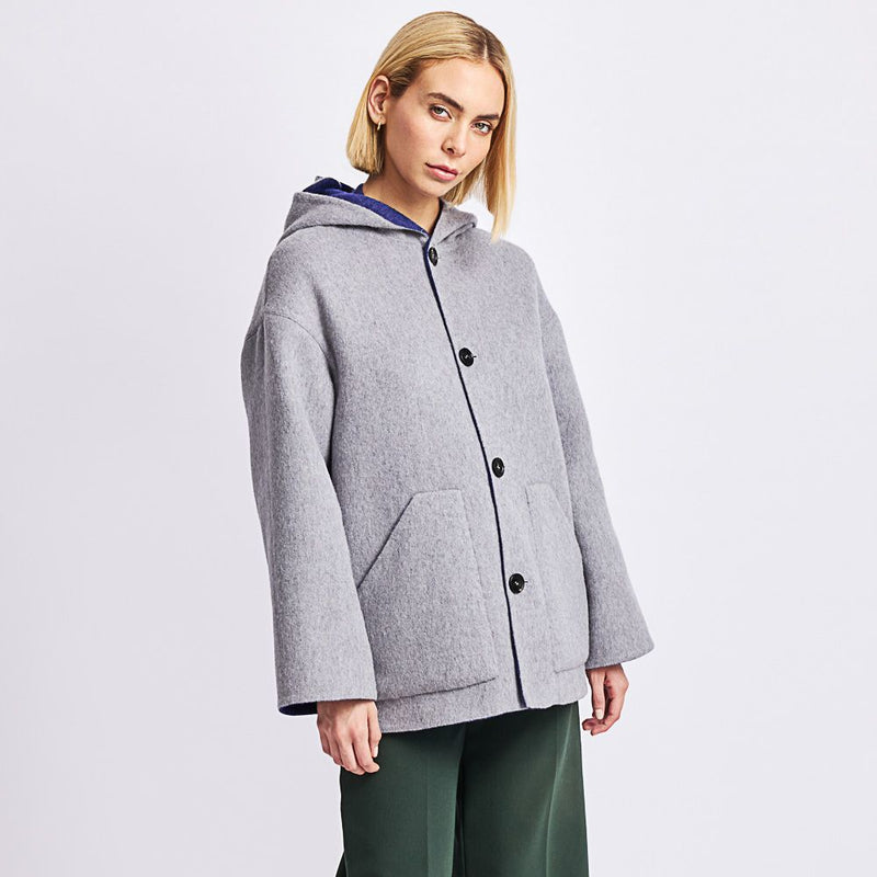 Kuna Whoopi Coat - model wearing grey hooded coat with blue lining, large pockets, and black buttons on a neutral background