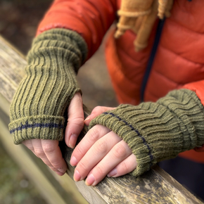Person wearing green fingerless gloves holding a wooden railing outdoors.