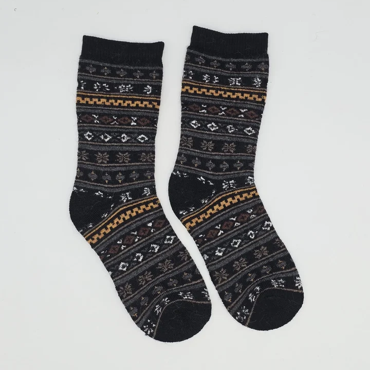 A pair of crew socks with a dark gray and black Nordic/Fair Isle pattern featuring brown, gold, and white geometric and floral motifs, displayed against a plain light gray background.