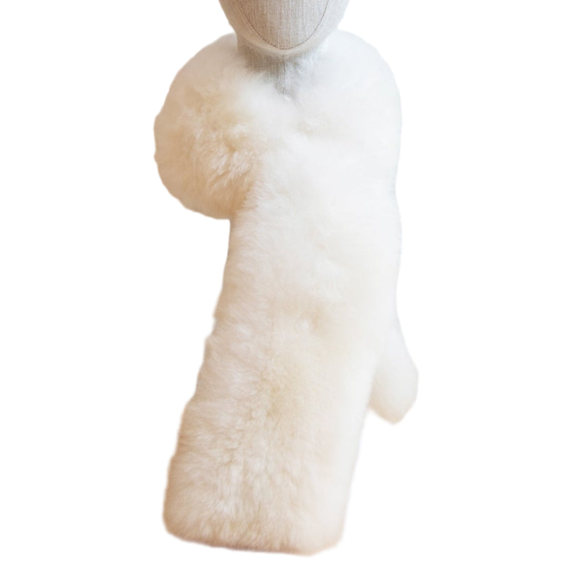 A white alpaca fur stole displayed against a white paneled wall on a wooden surface.