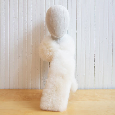 A white alpaca fur stole displayed against a white paneled wall on a wooden surface.