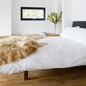 Samantha Holmes Alpaca Fur Throw - Cruelty-Free, a bed with a white bedspread and champagne-colored fur throw on the end in a white room