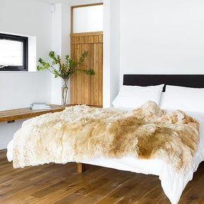 Samantha Holmes Alpaca Fur Throw - Cruelty-Free, a white bed with a beige alpaca fur throw on the end of the bed in a white room