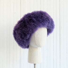 Premium Baby Alpaca Fur Hat. A purple Premium Baby Alpaca Fur Hat on a mannequin head against a white paneled background.