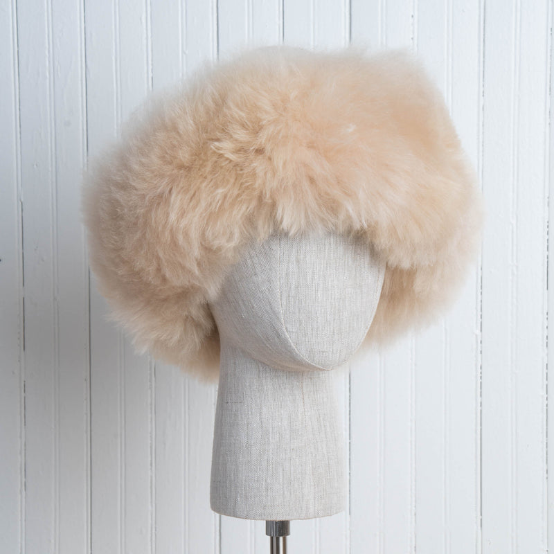 Premium Baby Alpaca Fur Hat. A beige Premium Baby Alpaca Fur Hat on a mannequin head against a white paneled background.