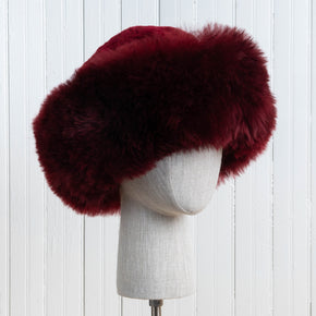 Premium Baby Alpaca Fur Hat. A Burgundy Premium Baby Alpaca Fur Hat on a mannequin head against a white paneled background.