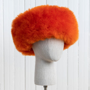 Premium Baby Alpaca Fur Hat. An orange Premium Baby Alpaca Fur Hat on a mannequin head against a white paneled background.