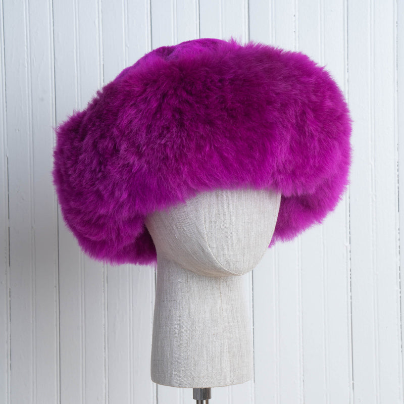 Premium Baby Alpaca Fur Hat. A fuchsia Premium Baby Alpaca Fur Hat on a mannequin head against a white paneled background.
