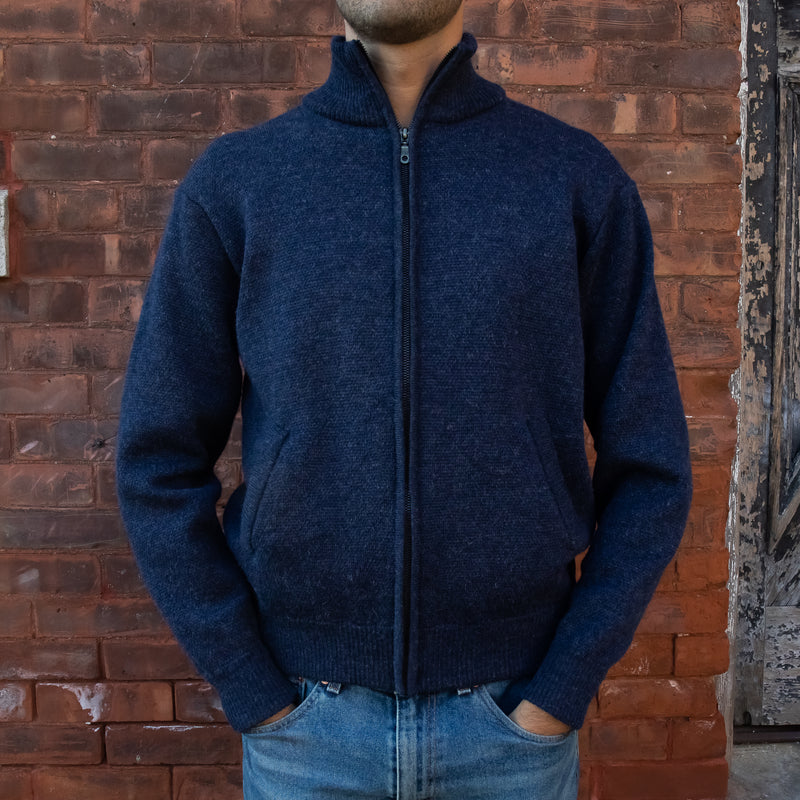 Men's Heavyweight Full-Zip 100% Baby Alpaca Wool Jacket, a man in a navy blue alpaca knitted hacket stands in front of a brick wall.
