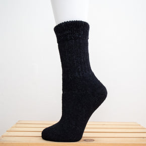 Andinista Alpaca Hiking Socks, a picture of a foot wearing a pair of black alpaca hiking socks on a wooden crate. 