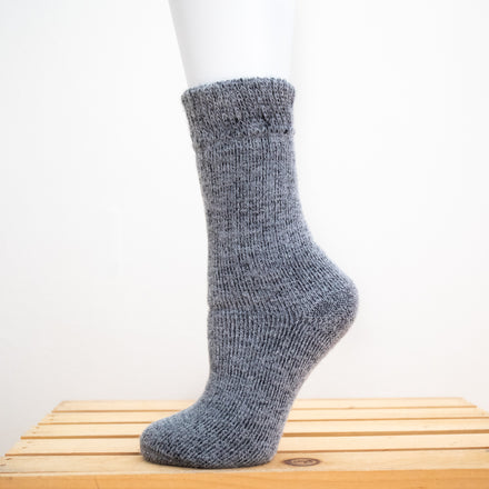 Andinista Alpaca Hiking Socks, a picture of a foot wearing a pair of grey alpaca socks on a wooden crate. 